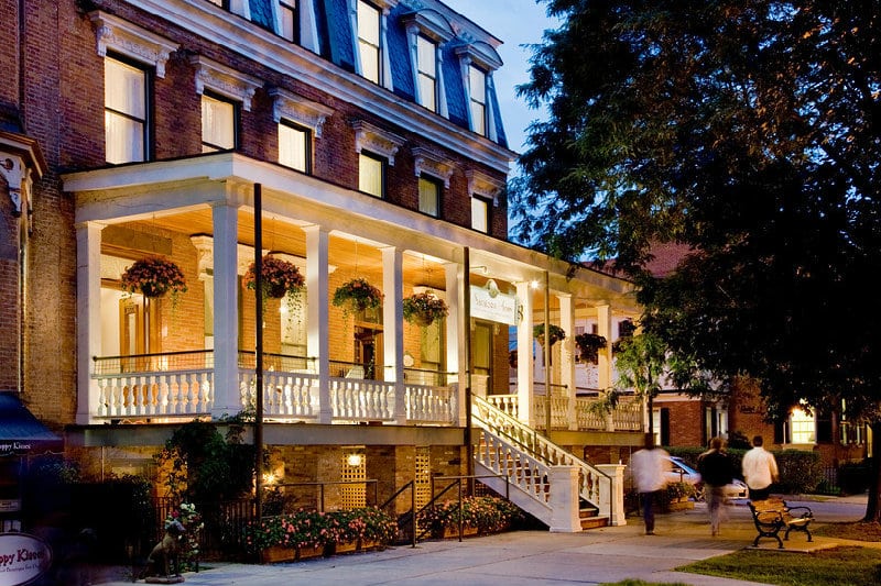 The grand porch of Saratoga Arms lit up on a summer evening, a welcoming sight in the heart of downtown Saratoga Springs