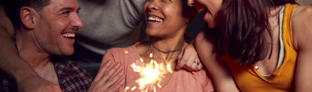 Two couples surround friend with cake and candles in front of her