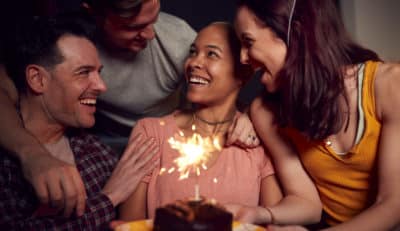 Two couples surround friend with cake and candles in front of her