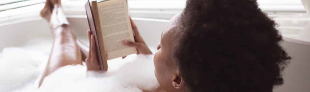 African American women soaking in bubble bath reading a book