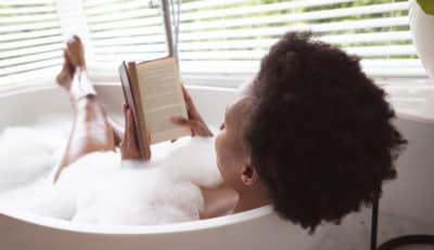 African American women soaking in bubble bath reading a book