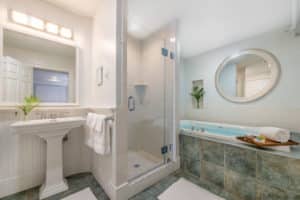 Glass enclosed tiled shower, two-person elevated whirlpool tub, pedestal white sink with framed mirror, tiled floor