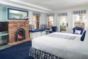 Large blue painted king room, brick fireplace, stand with flat screened tv, blue and white valence covers and match bedskirt