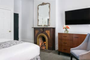 King Room with fireplace with framed mirror handling above mantel, flat screen tv hanging on wall above dresser