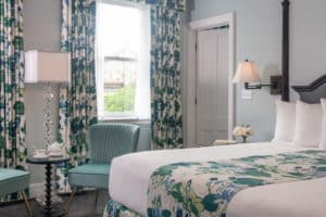 Blue walls in King room with cushioned blue chairs, Teal, green and cream full-length curtains and matching bedskirt.