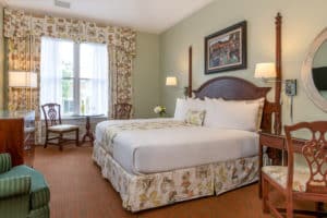 Light green painted walls with king bed, matching printed drapes and bedskirt, desk, green chair, round table by window