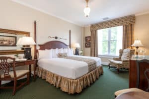 Cream room with two-poster king bed, gold drapes and matching bedskirt, queen anne chair by window