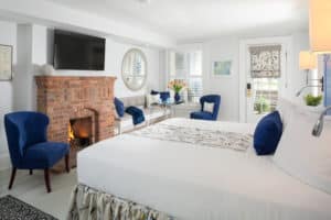 White King Room with brick fireplace, blue chairs, flat screen tv above mantel, private patio, flowers on windowsill