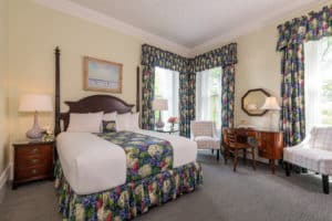 Cream queen room with cherry furniture, matching floral drapes and bedskirt, nighstands, desk and chairs by window