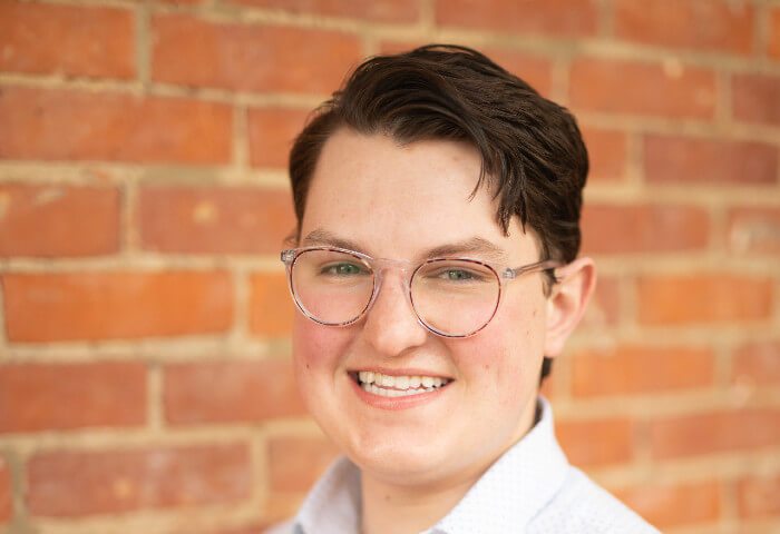 Headshot of smiling Aidan responsible for Sales and Guest Experience by red brick building