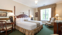 Cream room with two-poster king bed, gold drapes and matching bedskirt, queen anne chair by window