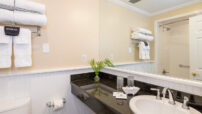 Long black marble shelf with inset white sink under mirror with reflection of white towels hanging on shelf