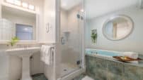 Glass enclosed tiled shower, two-person elevated whirlpool tub, pedestal white sink with framed mirror, tiled floor