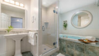 Glass enclosed tiled shower, two-person elevated whirlpool tub, pedestal white sink with framed mirror, tiled floor