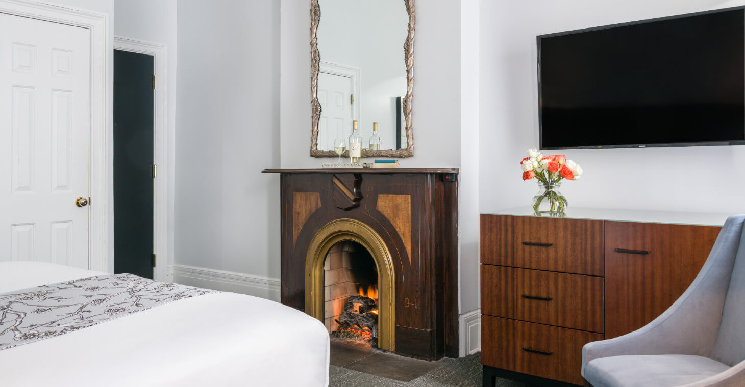 King Room with fireplace with framed mirror handling above mantel, flat screen tv hanging on wall above dresser