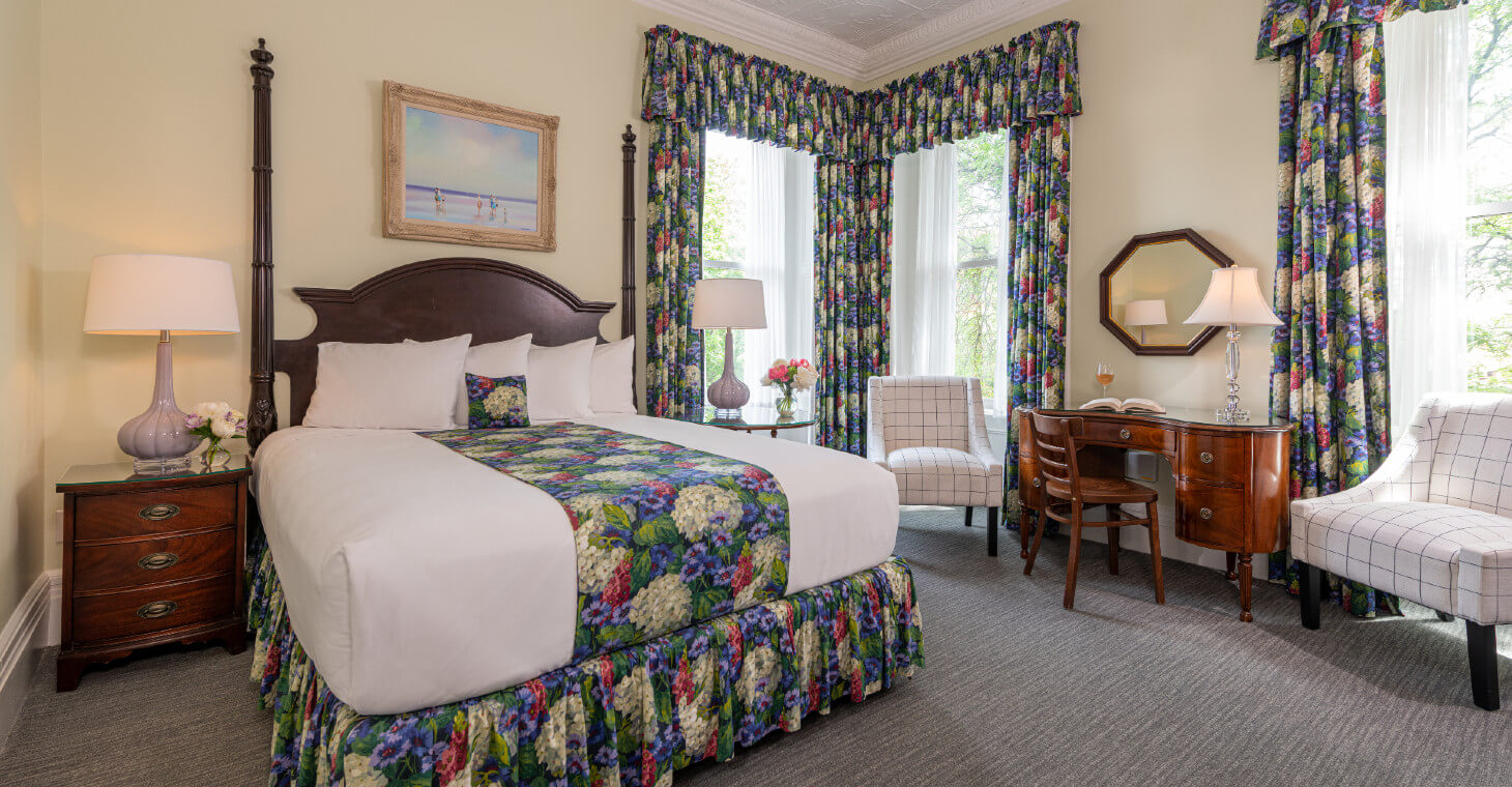 Cream queen room with cherry furniture, matching floral drapes and bedskirt, nighstands, desk and chairs by window