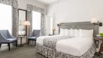 King room painted grey with headboard, cushioned chairs by windows, grey full-length curtains with matching bedskirt, nightstands
