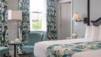Blue walls in King room with cushoned blue chairs, Teal, green and cream full-length curtains and matching bedskirt.