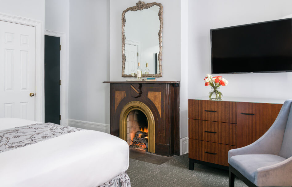 King Room with fireplace with framed mirror handling above mantel, flat screen tv hanging on wall above dresser