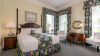 Cream queen room with cherry furniture, matching floral drapes and bedskirt, nighstands, desk and chairs by window