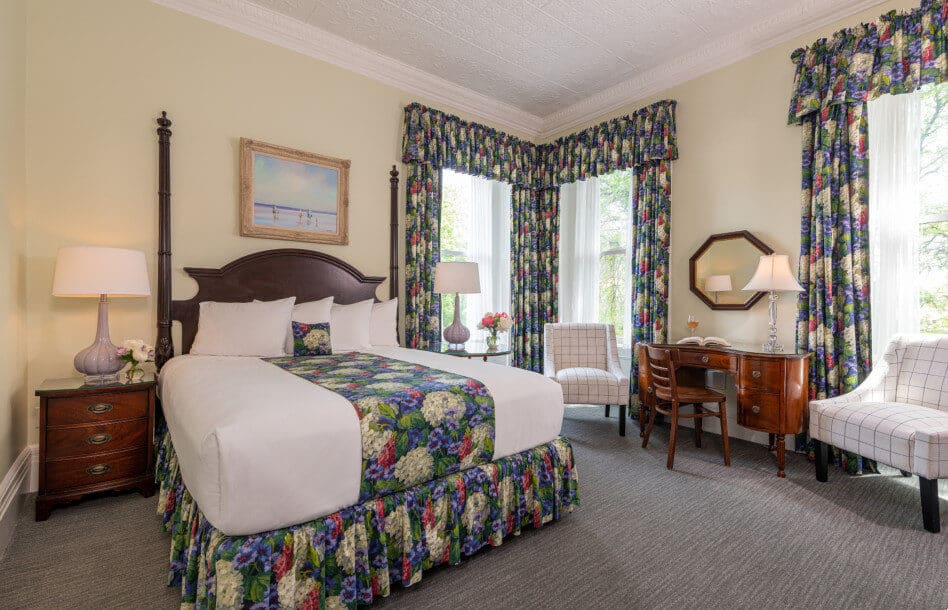 Cream queen room with cherry furniture, matching floral drapes and bedskirt, nighstands, desk and chairs by window