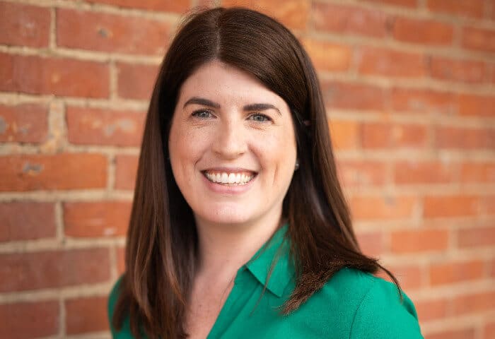 Headshot of smiling GM Rachel in green shirt by red brick building