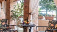 Floral cushioned chairs on terrace by metal table with white wine glasses, flower planter boxes on wall