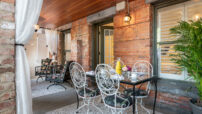 Glass table on terrace of red brick building set for breakfast, lounging chairs on opposite side by open door.