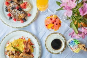 Aerial view of white and gold plates holding breakfast option, coffee mug and fruit bowl