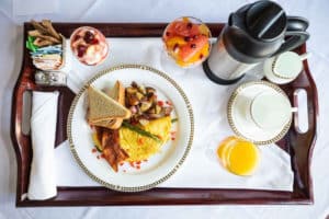 Room service brown wooden tray with breakfast including hot entree, OJ, coffee pitcher and fruit bowl