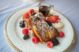 White porcelain plate with gold trim with powdered french toast garnished with raspberries and blueberries