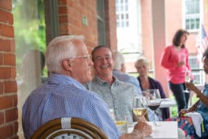 Close-up view of two smiling male guests visting on porch in evening with filled wine glasses