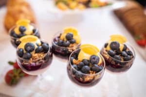 Glass fruit and yogurt cups holding blueberries, granola and organges on white linen cloth