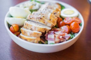 White porcelain bowl with salad with green, tomatoes, hard-boiled egg and sliced chicken