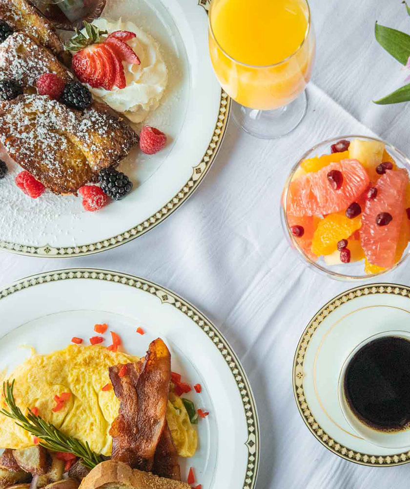 Breakfast spread of coffee, bacon and eggs, French Toast, and a bowl of mixed fruit.