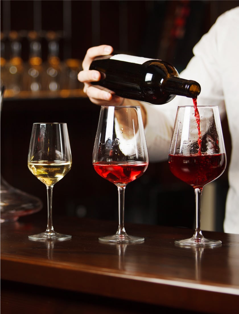 3 glasses of wine. The first glass is filled with white wine, second red, and the third a bottle is being poured into the glass with dark red wine.