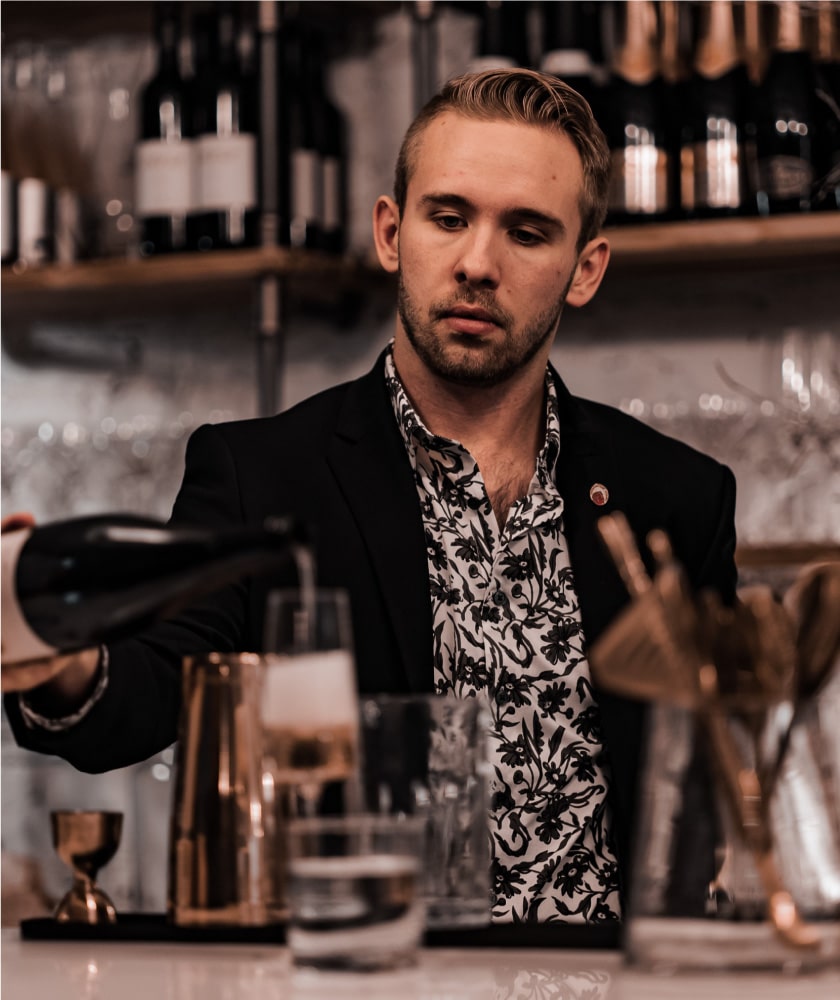 A young man pouring wine into a tall glass in a fancy restaurant