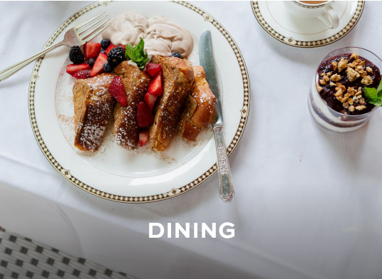 An overhead view of a plate of french toast with strawberries. There is a small glass of layered yoghurt and coffee next to the plate.