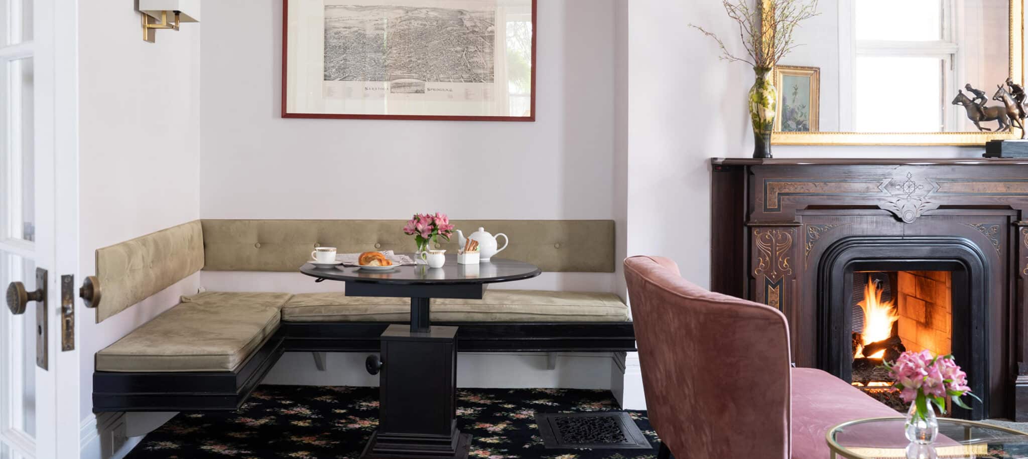 A yellow couch wrapped around a circular glass table. On the table is a vase with flowers and tea set.